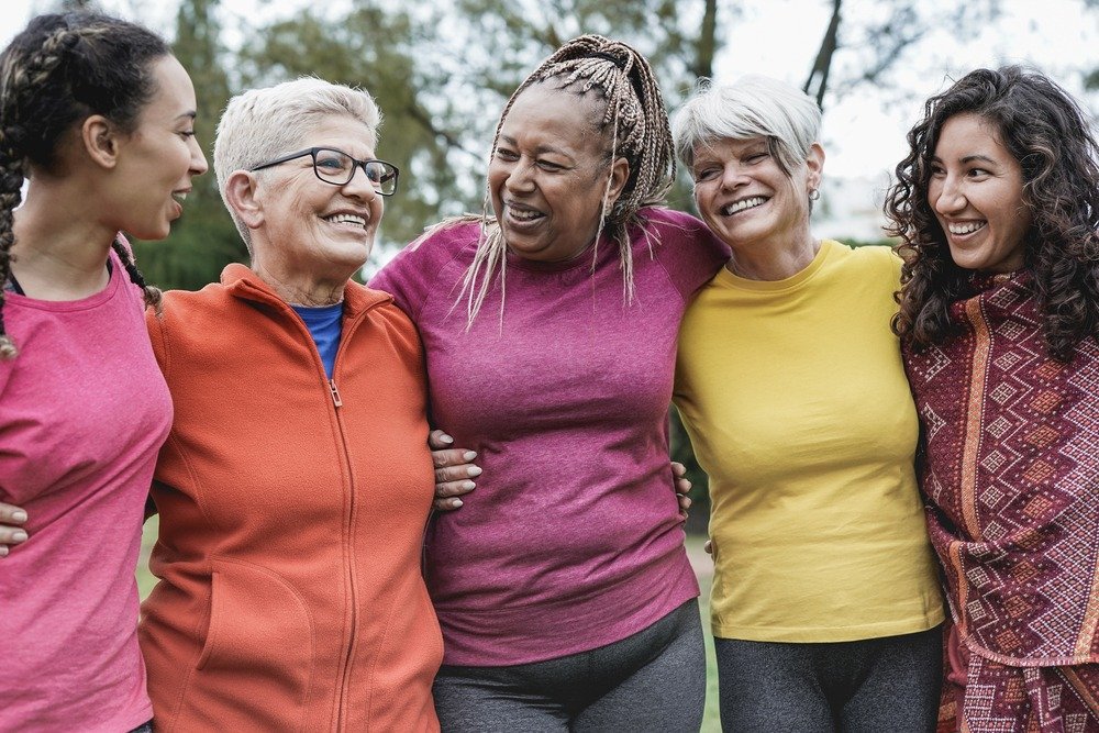 group of women of mixed race and age linked together holding each other
